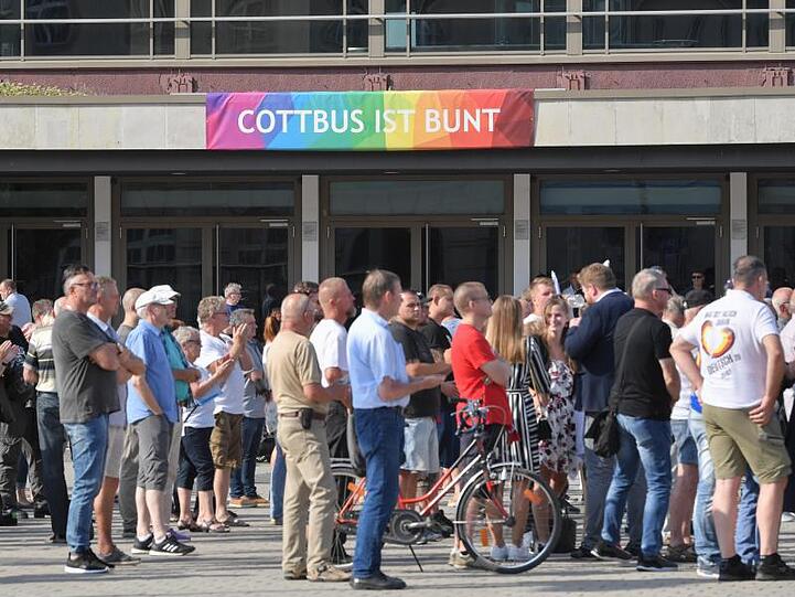 Teilnehmer des Wahlkampfauftakts der AfD-Jugendorganisation Junge Alternative stehen vor einem Transparent an der Stadthalle mit der Aufschrift "Cottbus ist bunt".