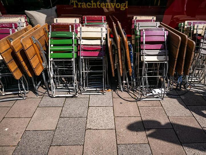 Zusammengestellte Tische und Stühle stehen vor einem Lokal im Gärtnerplatz-Viertel in München. Foto: Peter Kneffel/dpa/Archivbild