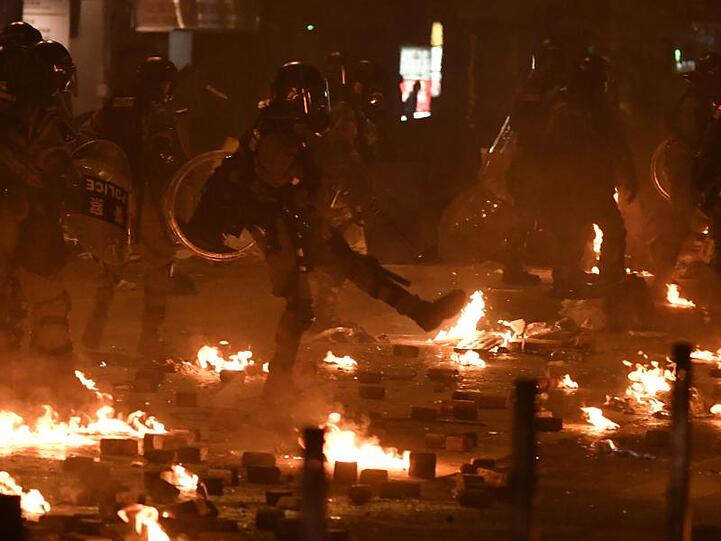 Polizisten in Schutzausrüstung stehen zwischen den Resten von Molotowcocktails.