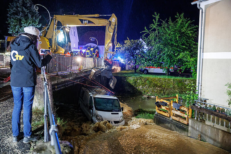 Kastl: Feuerwehrleute und ein Bagger arbeiten daran, einen Kastenwagen aus den Überflutungen vor einer Brücke zu bergen.