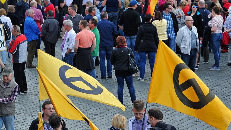 Demonstranten halten am Rande einer Pegida-Kundgebung Fahnen mit dem griechischen Buchstaben "Lambda", dem Symbol der identitären Bewegung (unten). Foto: Matthias Hiekel/Archiv