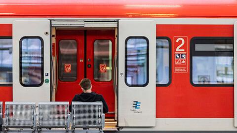 Ein Mann sitzt an einem Bahnhof vor einem Regionalzug auf der Bank.