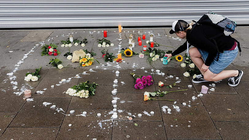 Passanten legen Blumen und Kerzen vor dem Supermarkt ab.