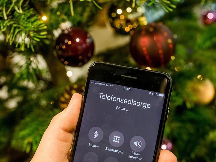 Mit einem Smartphone wird die Nummer der Telefonseelsorge vor einem Weihnachtsbaum gewählt. Foto: Michael Kappeler/Archiv