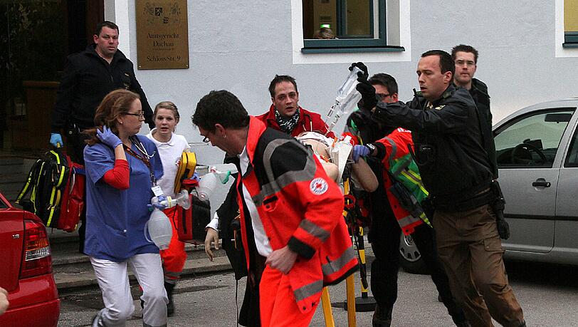 Bluttat in Dachau: Ein schwerverletzter 31-jähriger Staatsanwalt wird zum Notarztwagen gebracht. Im Gerichtssaal hatte ein Angeklagter erst auf den Richter gezielt. Dann schoss er drei Kugeln in den Oberkörper des Staatsanwalts. Der Mann stirbt auf dem Weg ins Krankenhaus. Bluttat in Dachau: Ein schwerverletzter 31-jähriger Staatsanwalt wird zum Notarztwagen gebracht. Im Gerichtssaal hatte ein Angeklagter erst auf den Richter gezielt. Dann schoss er drei Kugeln in den Oberkörper des Staatsanwalts. Der Mann stirbt auf dem Weg ins Krankenhaus.