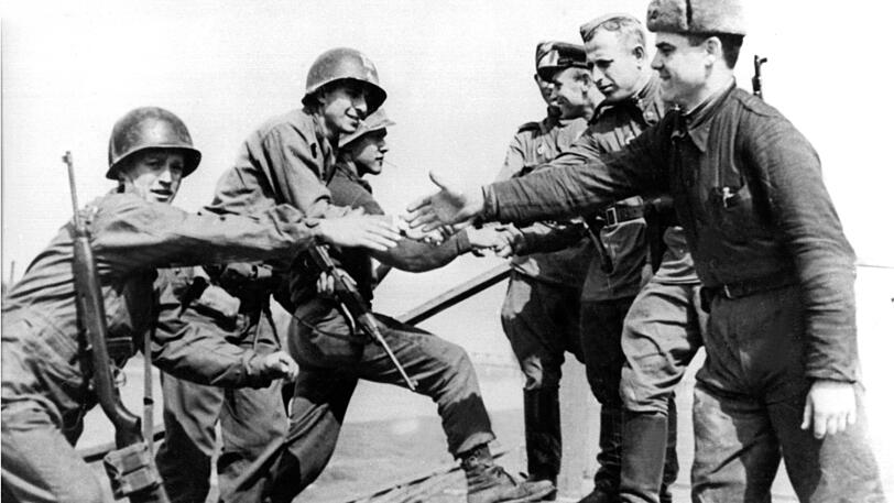 25. April 1945: Keine Politiker, sondern einfache Soldaten, die Weltgeschichte schreiben. US-amerikanische (l) und sowjetische Soldaten reichen sich auf den Trümmern einer Elbbrücke bei Torgau (Sachsen) die Hände.
