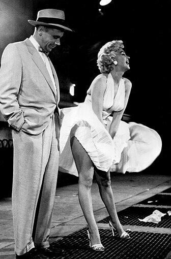Monroe steht mit weißem Kleid über einem Luftschacht in New York, wo ihr Rock hochgeweht wird. Neben ihr steht Schauspielerkollege Tom Ewell.