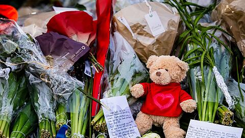 Menschen legen Blumen, Teddys und Botschaften am Brandort ab.