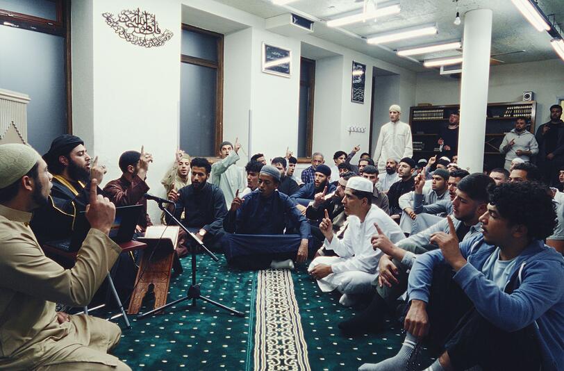 Prediger Abu Wala'a (Ibtasamm Shah, zweiter von links) unterrichtet seine Anhänger in der Moschee. Prediger Abu Wala'a (Ibtasamm Shah, zweiter von links) unterrichtet seine Anhänger in der Moschee.