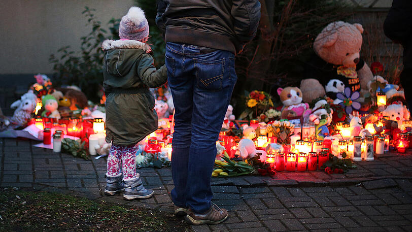 Ein Mädchen steht mit ihrem Vater vor Teddybären, Blumen und Kerzen, die in Herne (Nordrhein-Westfalen) vor einem Haus in einem Vorgarten liegen. Nach der Ermordung eines neunjährigen Jungen in Herne im Ruhrgebiet sucht die Polizei einen 19 Jahre alten Verdächtigen. zeigt einen dringend tatverdächtigen 19-jährigen Mann aus Herne.