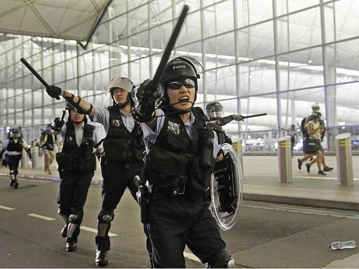 Polizisten mit Schlagstöcken im Hongkonger Flughafen an.