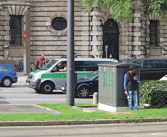 Die Polizei taucht auf, der Scheibenputzer versteckt sich blitzartig hinter einem Trafokasten.