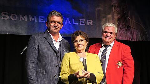 Gefeierte Preisträgerin des Sigi-Sommer-Talers: Monika Baumgartner mit der Trophäe, umrahmt von ihrem Laudator und Bergdoktor-Sohn Hans Sigl (l.) und Narrhalla-Präsident Günther Grauer.