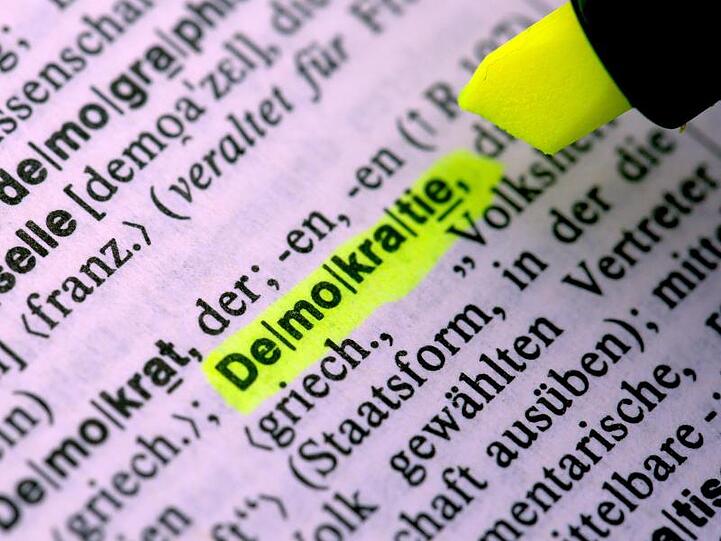 Jemand markiert im Duden das Wort "Demokratie". Foto: Federico Gambarini/Archivbild