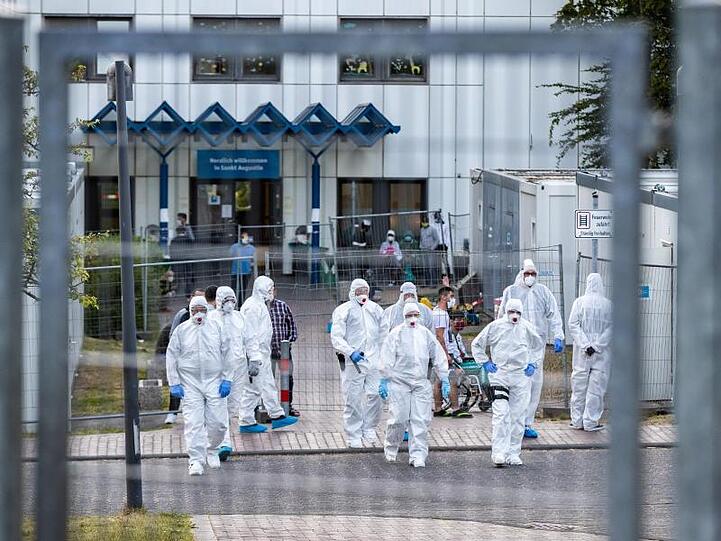 Beamte der Polizei und des Ordnungsamtes in Schutzanzügen vor der St. Augustiner Flüchtlingsunterkunft in NRW.