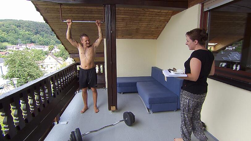 Jörg (32), der tätowierte Teilzeitbauer, wird am ersten Morgen von Vanessa (30) beim Oben-Ohne-Fitnesstraining auf dem Balkon erwischt.