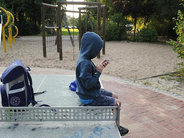 Ein Junge sitzt mit seinem Schulranzen auf einer Tischtennisplatte und spielt auf einem Smartphone. Foto: Jens Kalaene/dpa-Zentralbild/dpa/Archivbild