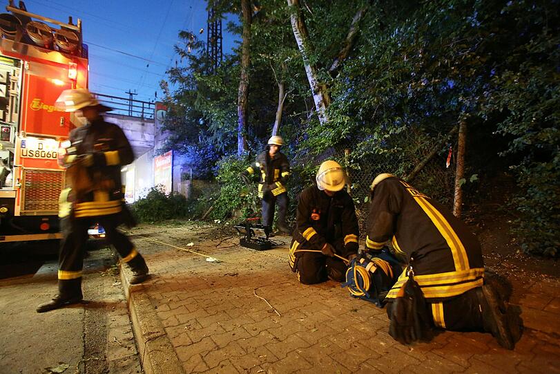 Feuerwehrleute arbeiten an einem Hang, hinter dem ein Baum auf ein Gartenhaus gestürtzt war und drei Menschen töte.