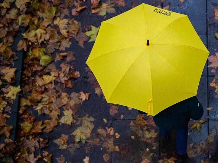 Eine Person läuft mit einem Regenschirm auf einem Gehweg. Foto: Tom Weller/dpa