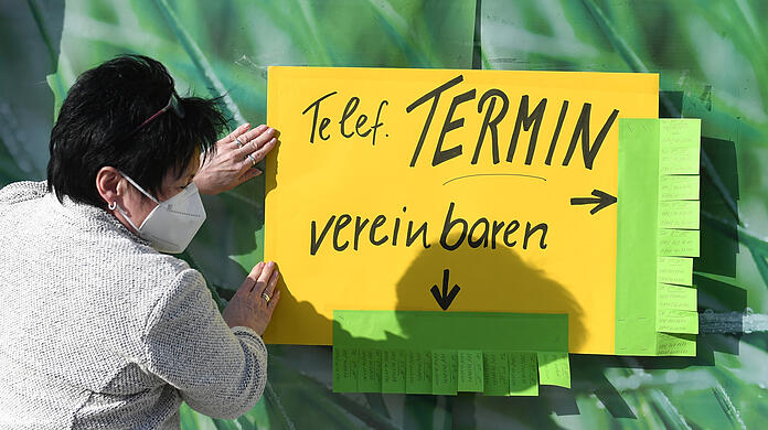 Eine Mitarbeiterin eines Schuhgeschäfts in der Münchner Innenstadt klebt ein Terminvereinbarungsschild aufs Schaufenster.