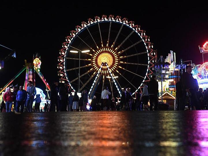 Oktoberfest 2019: Die Lichter der Wiesn und das Riesenrad spiegeln sich auf dem nassen Straße.