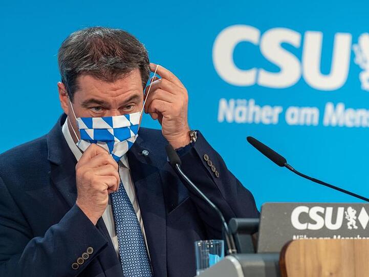 Markus Söder (CSU) steht auf einem Podium und setzt sich seine Mundschutzmaske auf. Foto: Peter Kneffel/dpa