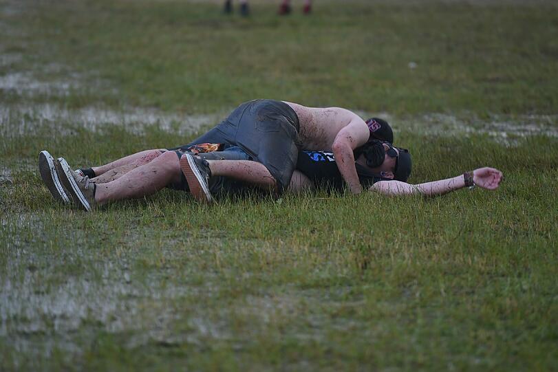 Zwei Festivalbesucher tollen sich bei Regen in einer Pfütze.