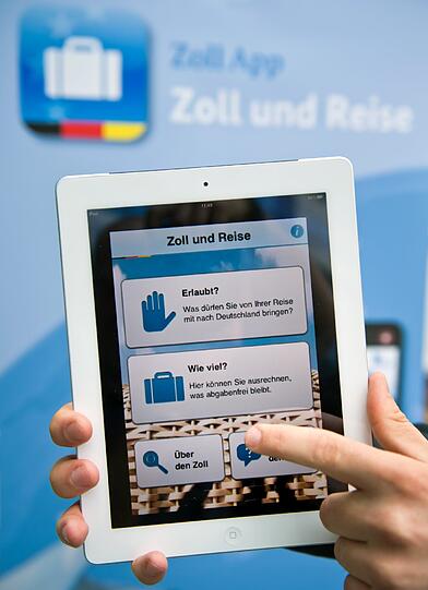 Ein Zollbeamter präsentiert am 01.07.2013, am Rande der Jahrespressekonferenz des deutschen Zolls auf dem Geländes des Flughafens Franz-Josef-Strauß bei München (Bayern), eine kostenlose App namens ?Zoll und Reise? für mobile Telefone und Tabletts, die Reisenden anzeigt wieviel Waren sie nach Deutschland einführen dürfen. Bei der Veranstaltung wurde die nationale Statistik, die Entwicklungen im internationalen Warenverkehr bei den Steuereinnahmen sowie in der Kriminalitätsbekämpfung bei Produktpiraterie und Artenschutz präsentiert.