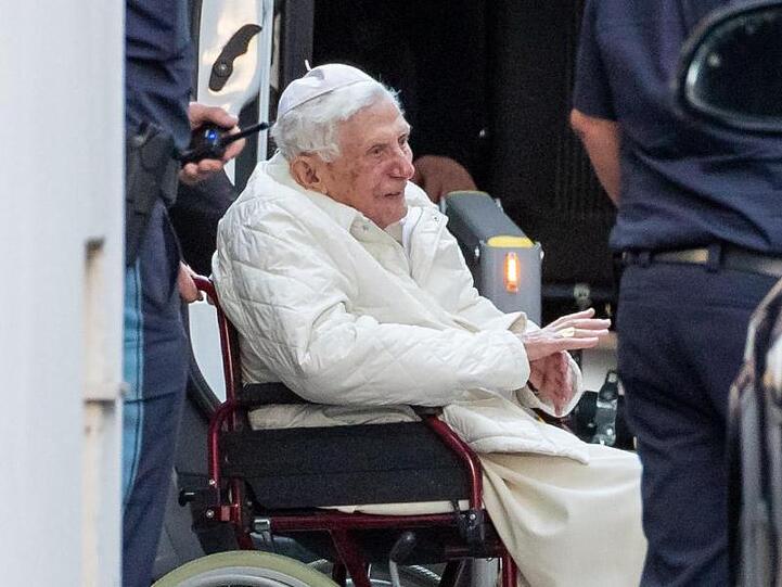 Der emeritierte Papst Benedikt XVI wird mit einem Rollstuhl in einen Bus geschoben. Foto: Daniel Karmann/dpa/Archivbild