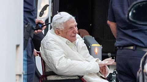 Der emeritierte Papst Benedikt XVI wird mit einem Rollstuhl in einen Bus geschoben. Foto: Daniel Karmann/dpa/Archivbild