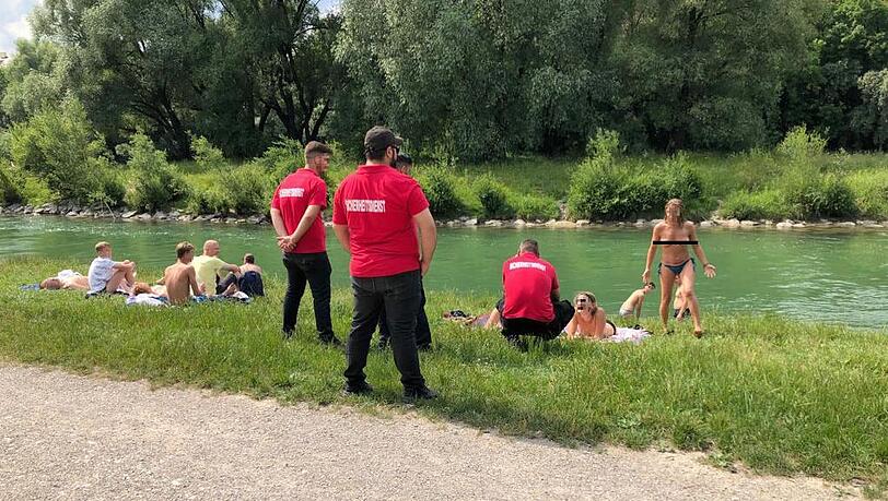 Männer mit "Sicherheitsdienst"-T-Shirts sprechen Frauen ohne Bikini-Oberteil an der Isar an.