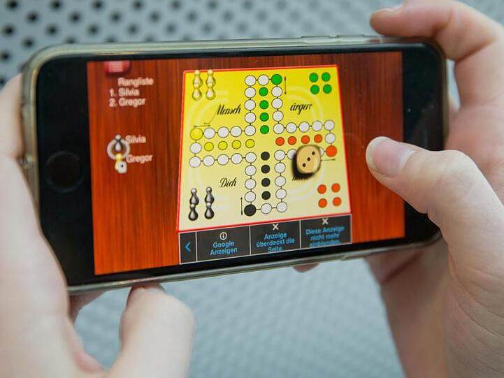 Eine Frau spielt "Mensch ärgere Dich nicht" auf einem Smartphone.