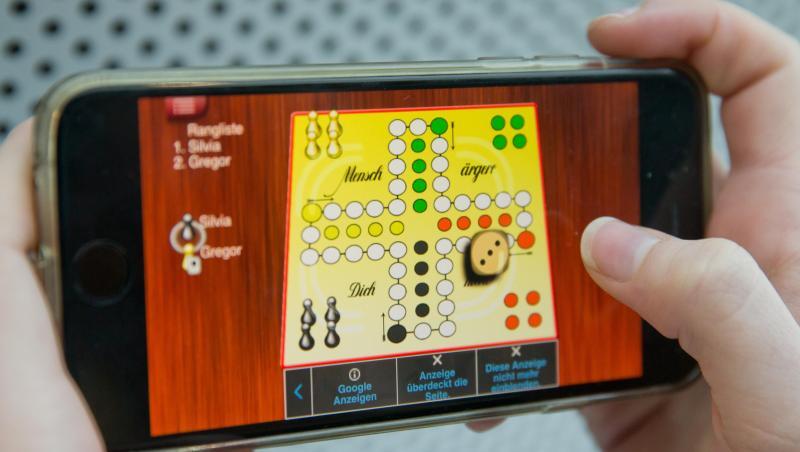 Eine Frau spielt "Mensch ärgere Dich nicht" auf einem Smartphone. Eine Frau spielt "Mensch ärgere Dich nicht" auf einem Smartphone.