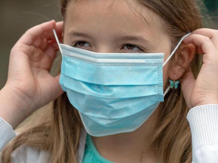 Eine Schülerin setzt sich vor dem Betreten eines Schulgeländes in Frankfurt am Main eine Einweg-Maske auf.