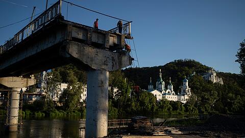 Bauarbeiter steigen von einer Leiter auf einer zerstörten Brücke neben dem Kloster Swjatohirsk herunter.