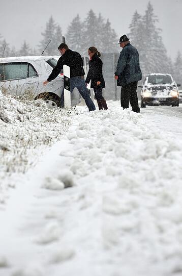 Drei Personen schieben am Samstag auf der Straße von Schliersee (Oberbayern) nach Spitzingsee ein Auto an den Straßenrand, das im Schnee stecken geblieben war.