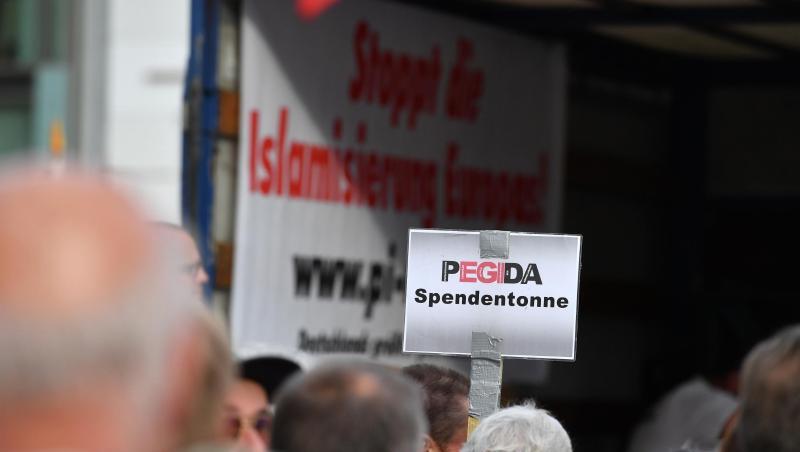 Auf einer Kundgebung von Pegida halten Anhänger ein Schild mit dem Schriftzug "Pegida Spendentonne" in die Höhe.