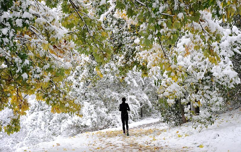 Eine Joggerin läuft am Sonntagmorgen durch den verschneiten Olympiapark in München.