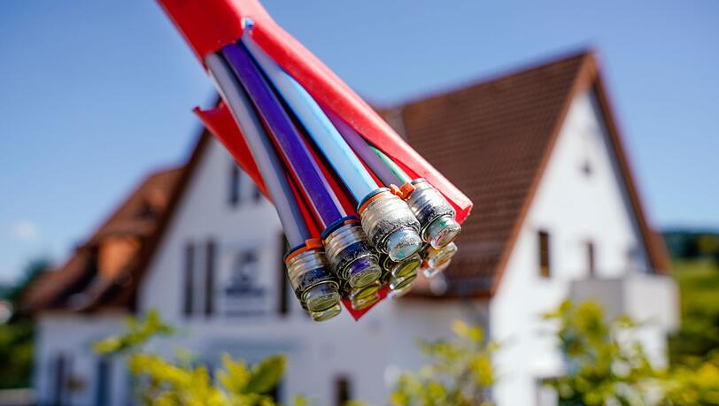 Ein Bündel mit Umhüllungen für Glasfaserkabel hängt vor einem Wohnhaus.