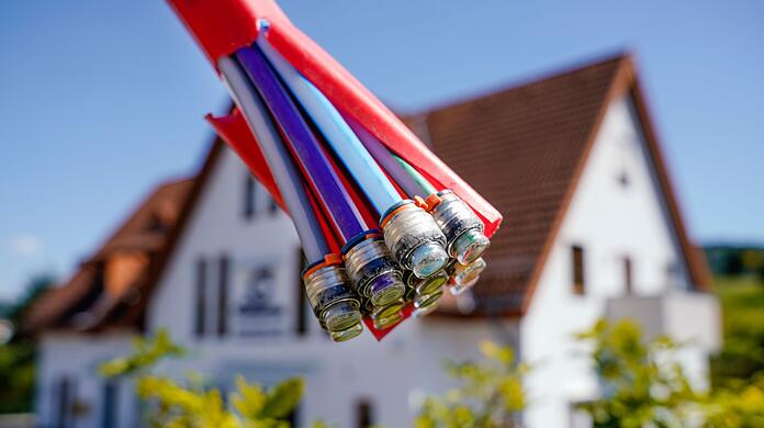 Ein Bündel mit Umhüllungen für Glasfaserkabel hängt vor einem Wohnhaus.