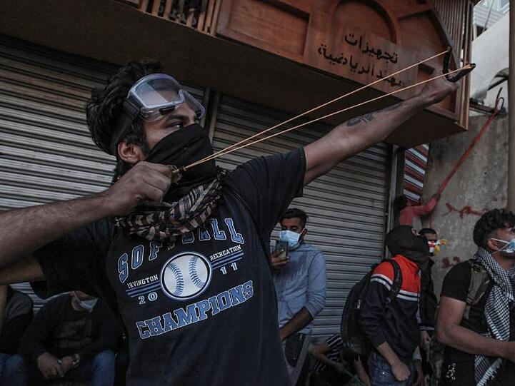 Ein Demonstrant in Bagdad zielt mit einer Steinschleuder auf Einsatzkräfte.