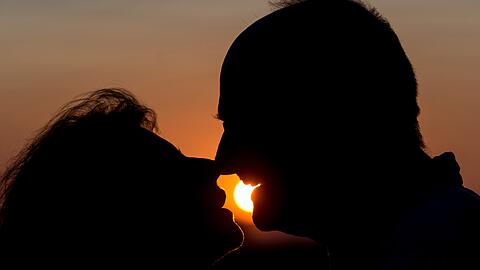 Ein Senioren-Paar küsst sich im Sonnenuntergang.
