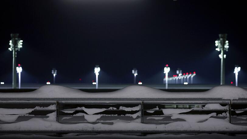 Flutlichter stehen hinter einem schneebedeckten Parkhaus am Münchener Flughafen.