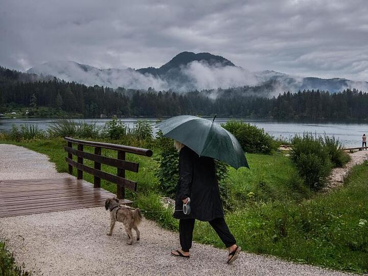 Eine Frau geht bei Regen mit ihrem Hund am Hintersee in Ramsau Bei Berchtesgaden spazieren.