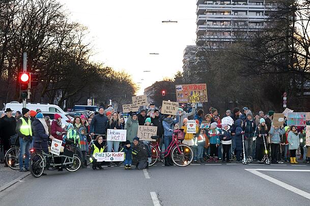 Rund 200 Eltern und Kinder demonstrieren Donnerstag früh vor Schulbeginn für einen Umbau der Karl-Theodor-Straße. Die Pläne dafür liegen schon seit Jahren vor, im Februar diskutiert der Stadtrat erneut darüber.