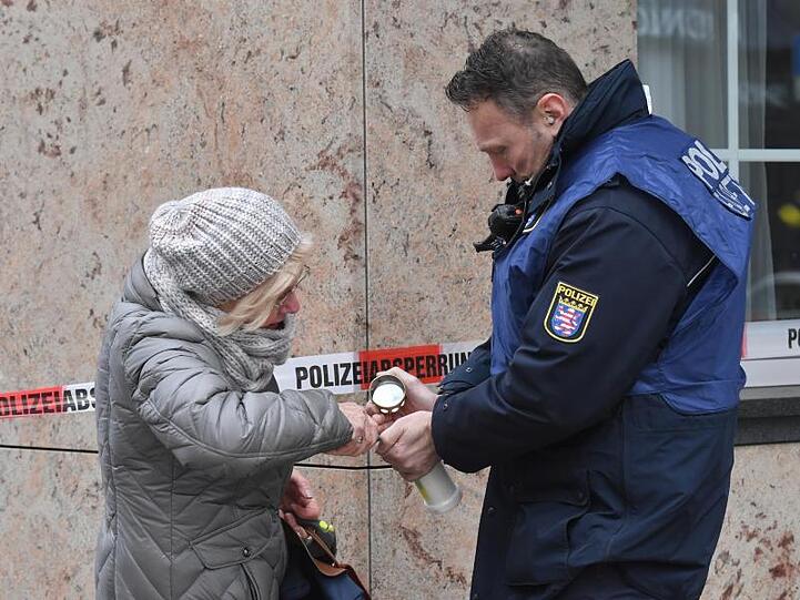 Ein Polizist hilft einer älteren Frau in der Nähe eines Tatortes am Heumarkt, eine Kerze anzuzünden.