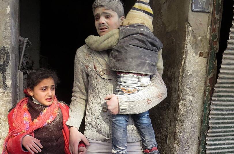 Ein Vater tritt mit seinen zwei Kindern nach einem Bombardement durch Regierungstruppen in der syrischen Stadt Aleppo aus dem Haus.