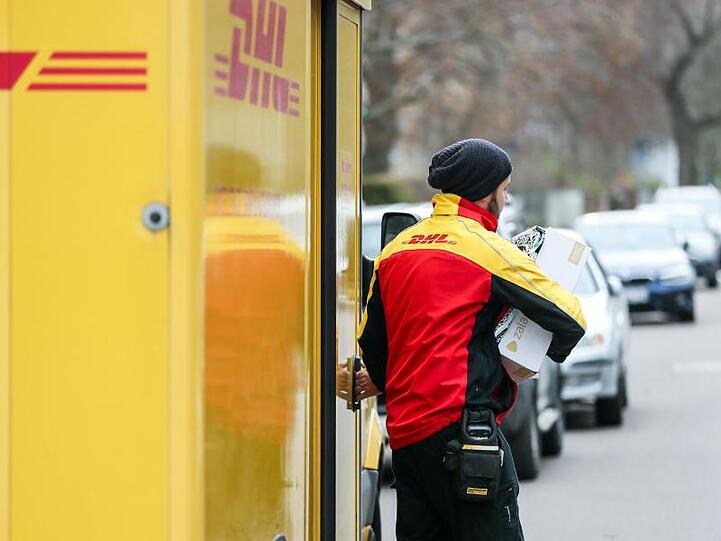 Ein DHL-Paketzusteller verlässt mit mehreren Sendungen sein Fahrzeug.