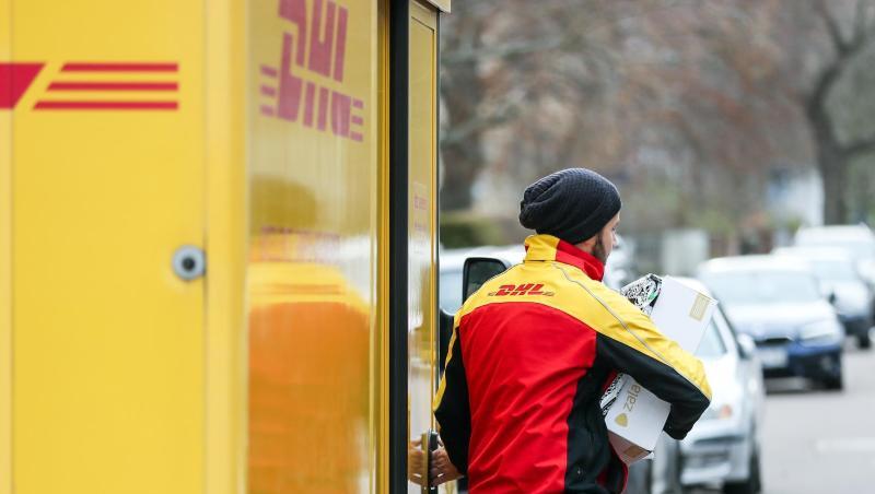 Ein DHL-Paketzusteller verlässt mit mehreren Sendungen sein Fahrzeug. Ein DHL-Paketzusteller verlässt mit mehreren Sendungen sein Fahrzeug.