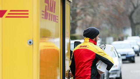 Ein DHL-Paketzusteller verlässt mit mehreren Sendungen sein Fahrzeug.